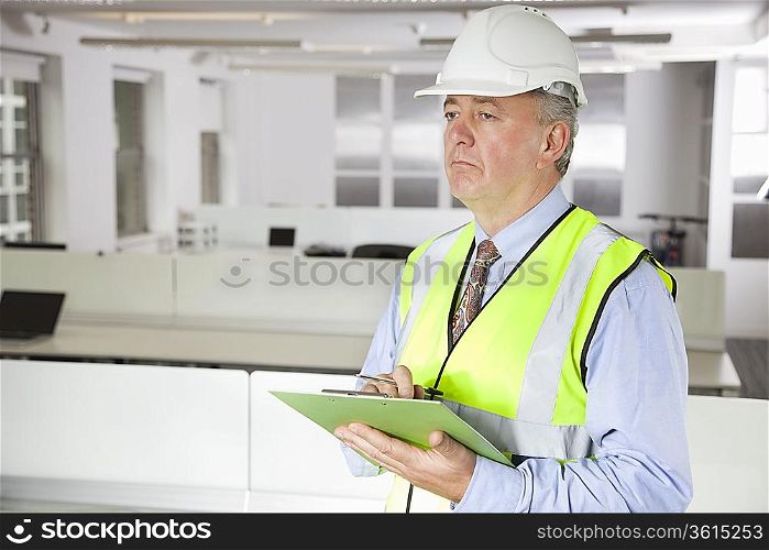 Middle-aged man in reflector vest and hard hat with clipboard at office