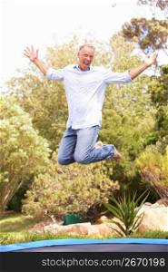 Middle Aged Man Jumping On Trampoline In Garden