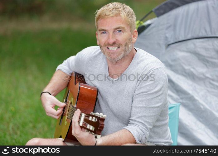 middle aged man playing guitar by his tent