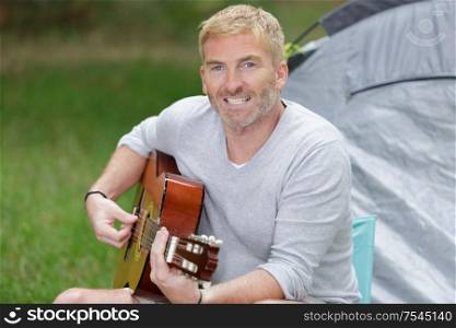 middle aged man playing guitar by his tent