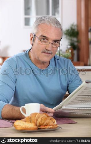 Middle-aged man reading newspaper whilst eating breakfast