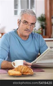 Middle-aged man reading newspaper whilst eating breakfast