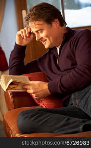 Middle Aged Man Relaxing With Book Sitting On Sofa