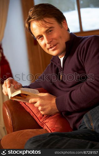 Middle Aged Man Relaxing With Book Sitting On Sofa