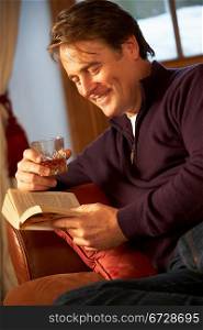 Middle Aged Man Relaxing With Book Sitting On Sofa Drinking Whisky