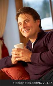 Middle Aged Man Relaxing With Hot Drink On Sofa Watching TV