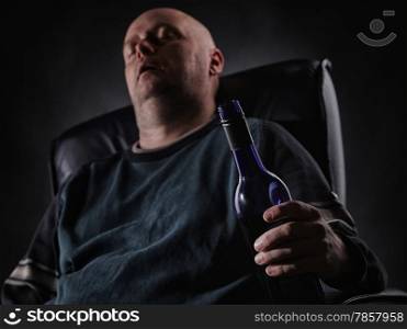 Middle aged man sleeps on an armchair and he holding a wine bottle, horizon format