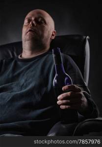 Middle aged man sleeps on an armchair and he holding a wine bottle, vertical format