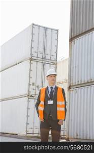 Middle-aged man standing against cargo containers in shipping yard