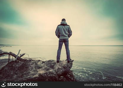 Middle-aged man standing on broken tree on wild beach looking at sea far horizon. Vintage, conceptual. . Middle-aged man standing on broken tree on wild beach looking at sea horizon