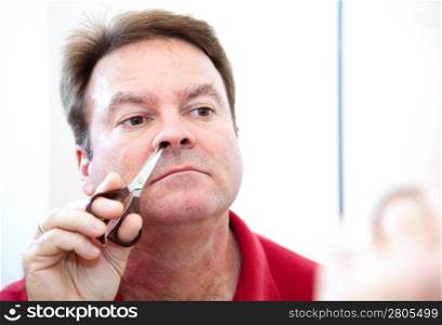 Middle aged man trimming his nose hair with grooming scissors.