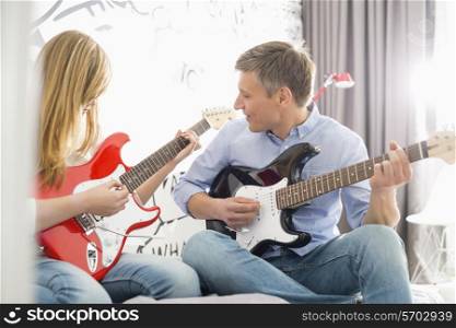 Middle-aged man with daughter playing guitars at home