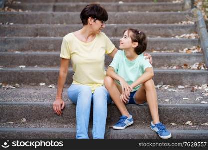 Middle-aged mother and daughter sit on the street on urban steps.. Middle-aged mother and daughter sit on the street