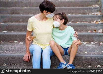 Middle-aged mother and daughter sit on the street wearing masks because of the Covid-19 pandemic. Middle-aged mother and daughter sit on the street wearing masks