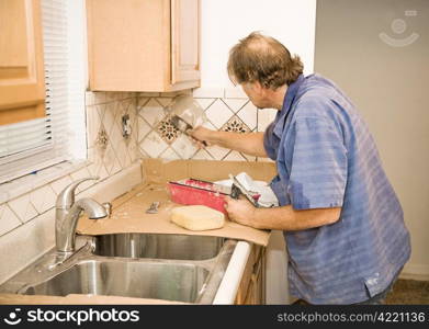 Middle aged tile-setter applying grout to kitchen tiles.