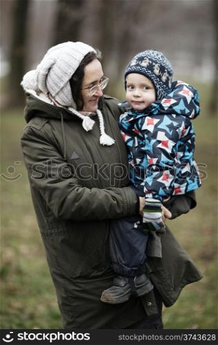 Middle-aged woman holding her cute young son in her arms on a cold winter day both dressed in thick warm winter clothes as they smile at the camera