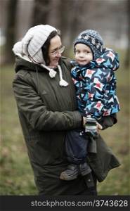 Middle-aged woman holding her cute young son in her arms on a cold winter day both dressed in thick warm winter clothes as they smile at the camera