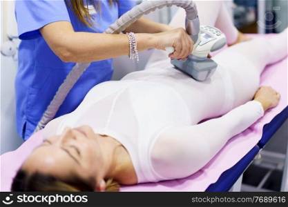 Middle-aged woman in special white suit having a anti cellulite belly massage with spa apparatus. Woman in special suit having a anti cellulite belly massage with spa apparatus