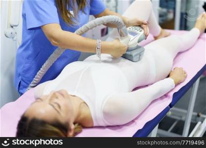 Middle-aged woman in special white suit having a anti cellulite belly massage with spa apparatus. Woman in special suit having a anti cellulite belly massage with spa apparatus