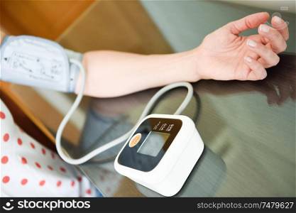 Middle-aged woman measuring her own blood pressure with an electronic blood pressure measurement device at home. Woman measuring her own blood pressure at home.