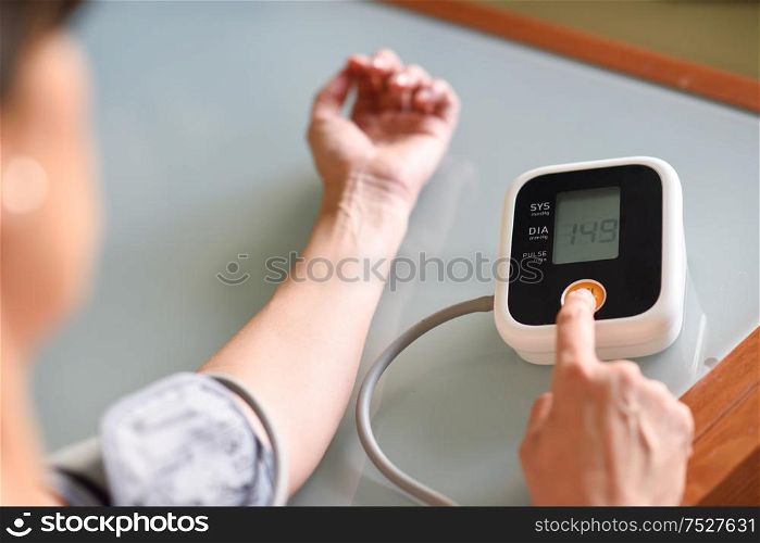 Middle-aged woman measuring her own blood pressure with an electronic blood pressure measurement device at home. Woman measuring her own blood pressure at home.
