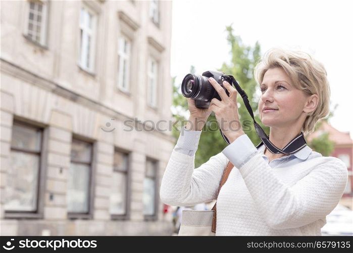 Middle-aged woman photographing through digital camera in city