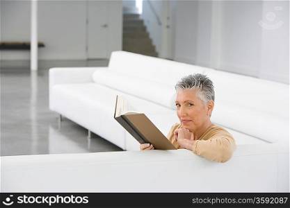 Middle-aged woman reading book on sofa