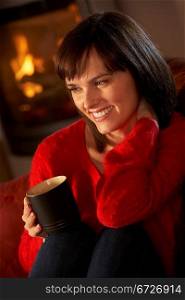Middle Aged Woman Relaxing With Hot Drink By Cosy Log Fire