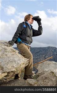 Middle-aged woman standing on rock and using binoculars