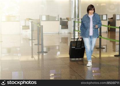 middle aged woman traveling in casual clothes. Female in airport with suitcase and passport going after check-in desk in for her flight. Passenger travel abroad on holiday or weekend. middle aged woman traveling in casual clothes. Female in airport with suitcase and passport going after check-in desk in for her flight. Passenger travel abroad on holiday or weekend.