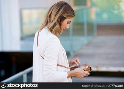 Middle-aged woman using her smartphone through a handbag with space to touch the touch screen. Caucasian female on urban background.. Middle-aged woman using her smartphone through a handbag with space to touch the touch screen.