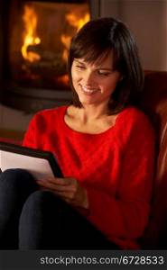 Middle Aged Woman Using Tablet Computer By Cosy Log Fire