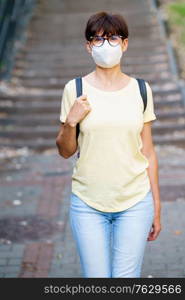 Middle-aged woman walking in a city park in summer wearing KN95 mask. Beautiful Middle-aged woman walking down the street
