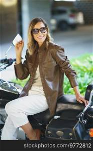 Middle aged woman with sunglasses sitting on a vintage motorcycle. Caucasian female in urban background.. Middle aged woman sitting on a vintage motorcycle. Caucasian female in urban background.
