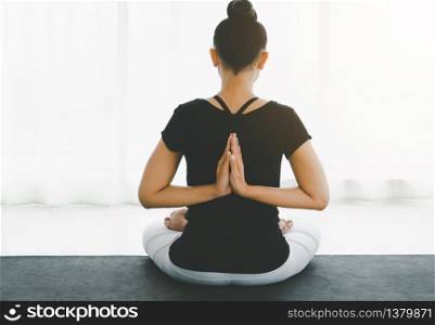 Middle aged women practicing yoga in Lotus pose or Padmasana with raised hands namaste behind the back. Meditation with yoga in white bedroom after wake up in the morning. Concept of exercise, relaxation and healthcare.