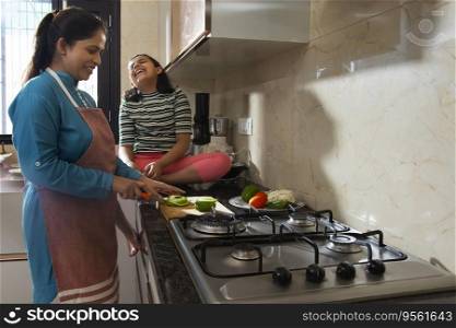 Middle class Indian woman chopping vegetables and her daughter sitting  beside her in kitchen
