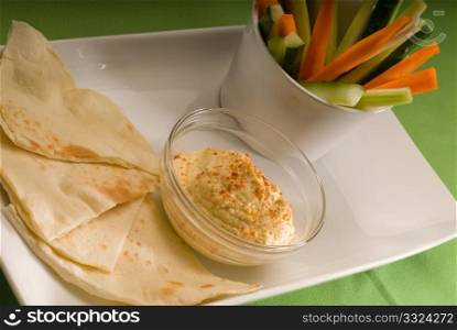 middle eastern hummus dip on a glass bowl with homemade pita bread and raw vegetable