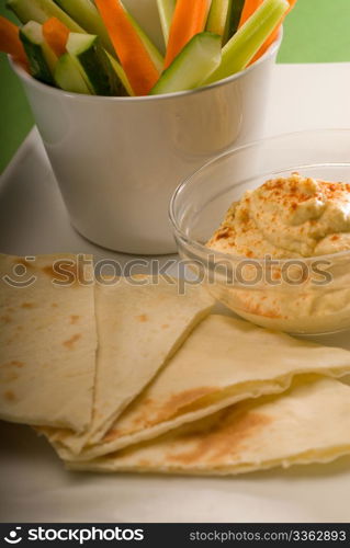 middle eastern hummus dip on a glass bowl with homemade pita bread and raw vegetable