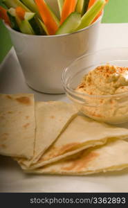 middle eastern hummus dip on a glass bowl with homemade pita bread and raw vegetable