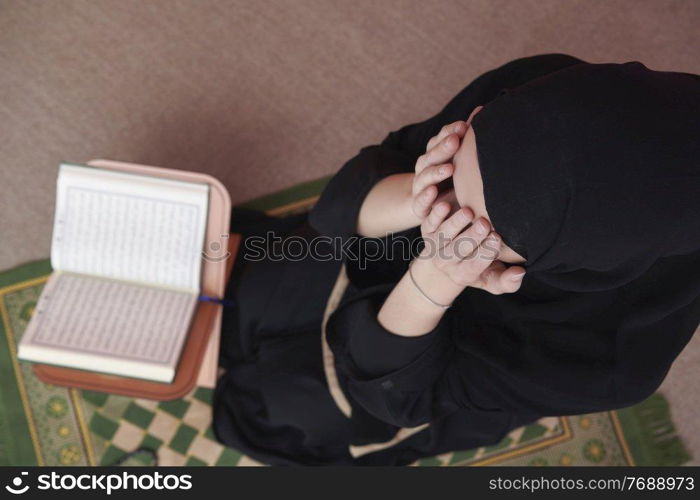 Middle eastern woman praying and reading the holy Quran, public item of all muslims. Education concept of Muslim woman studying The holy Quran at home or mosque in ramadan month.