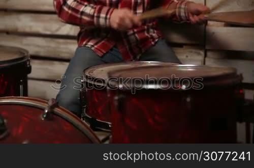 Middle section of musician playing drum set while jamming with rock band in the club. Close up of hands with drumsticks hitting drum and cymbal at concert in colorful spotlights.