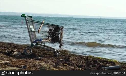 Middle shot of abandoned metal shopping trolley on the beach standing at the edge of the water in evening light