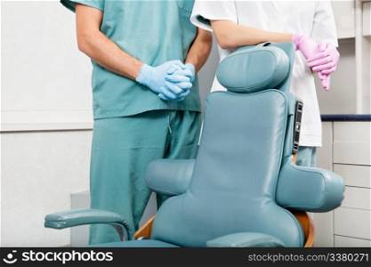 Midsection of a dentist and female assistant in exam room by dentist&rsquo;s chair. Dentist and female assistant in exam room by dentist&rsquo;s chair