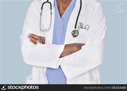Midsection of a doctor with arms crossed over light blue background