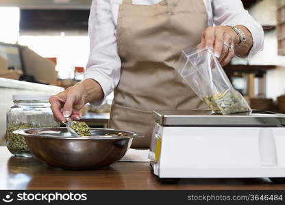 Midsection of an employee measuring ingredient on weight scale in spice store