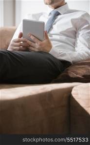 Midsection of businessman holding digital tablet on sofa at home