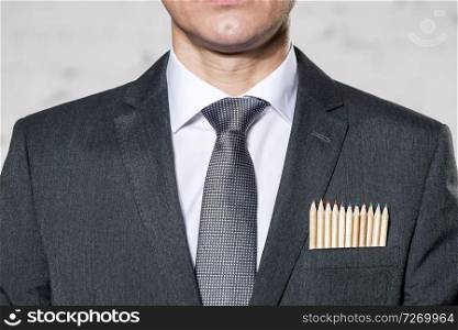 Midsection of businessman with colored pencils in pocket against wall