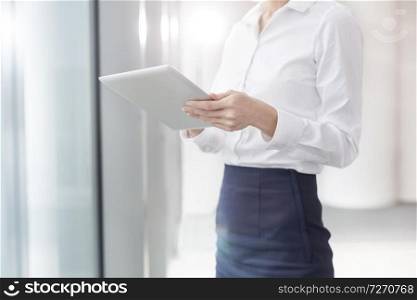 Midsection of businesswoman using digital tablet while standing in boardroom at office