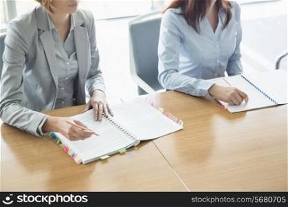 Midsection of businesswomen with books at table in office