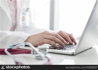 Midsection of doctor using laptop at table in hospital